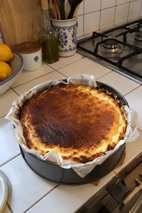 Tarta de queso recién horneada enfriándose en la encimera de una cocina con azulejos blancos