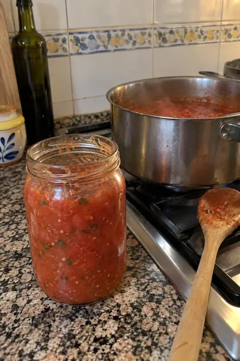Tarro de tomate frito casero y olla en el fuego en una cocina con azulejos